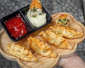Bánh mandu chiên hấp dẫn bày trên khay gỗ, một chiếc bánh được chấm ngập trong sốt mayonnaise