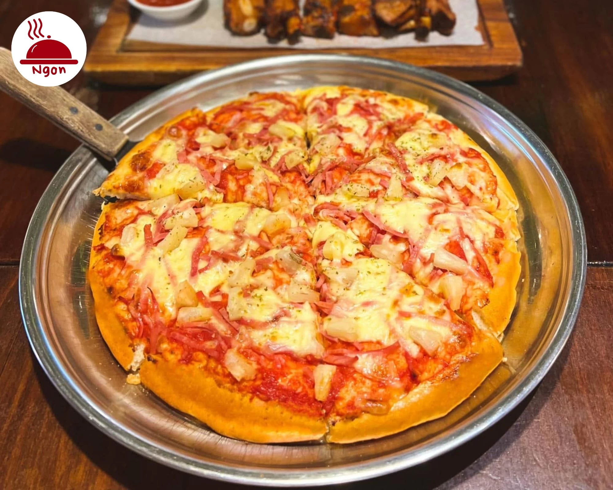 Cận cảnh chiếc bánh pizza nóng hổi phủ đầy thịt nguội và dứa tươi ngon trên khay kim loại tại Al Fresco's